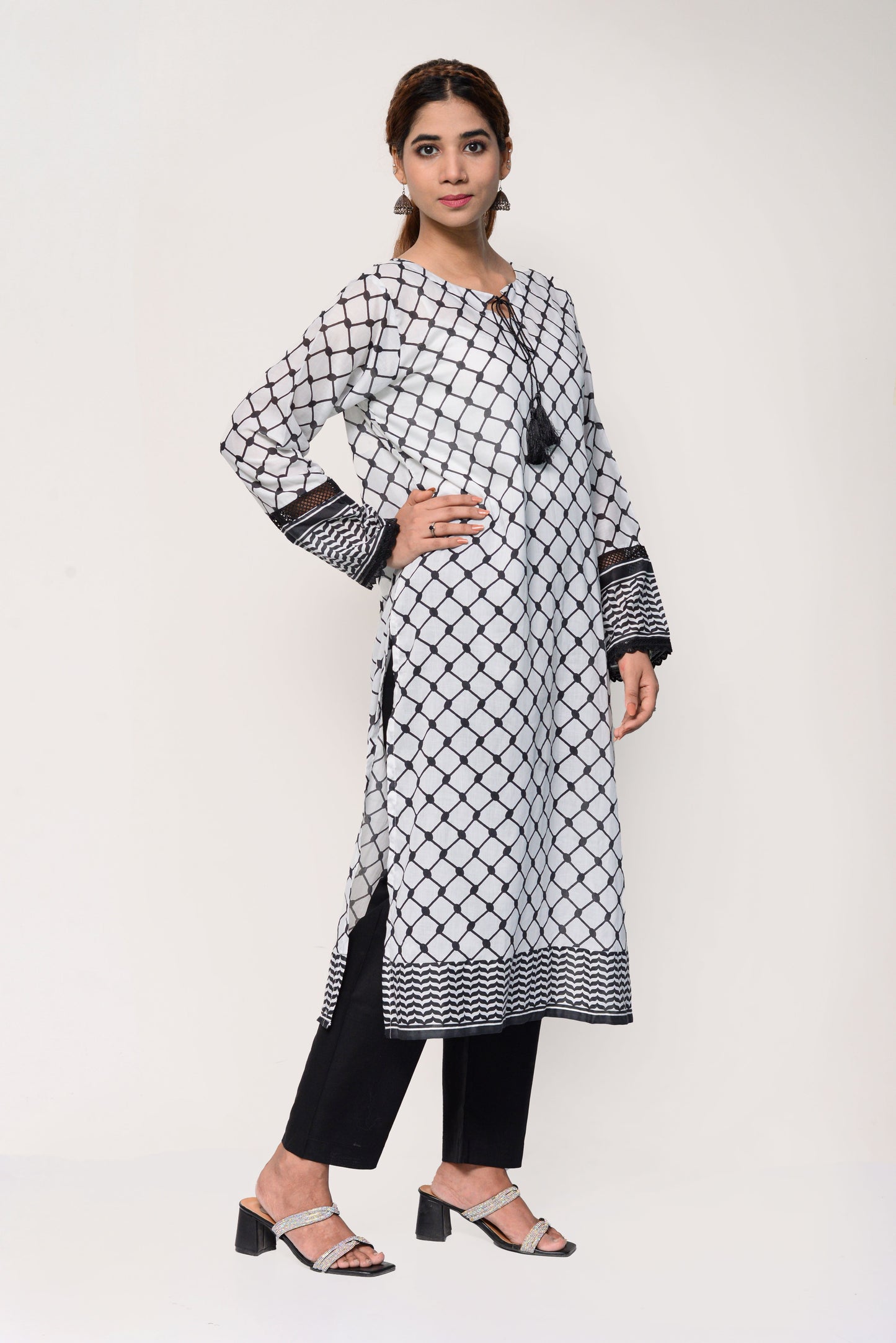 Woman wearing a black and white Keffiyah patterned long shirt with black pants on a white background