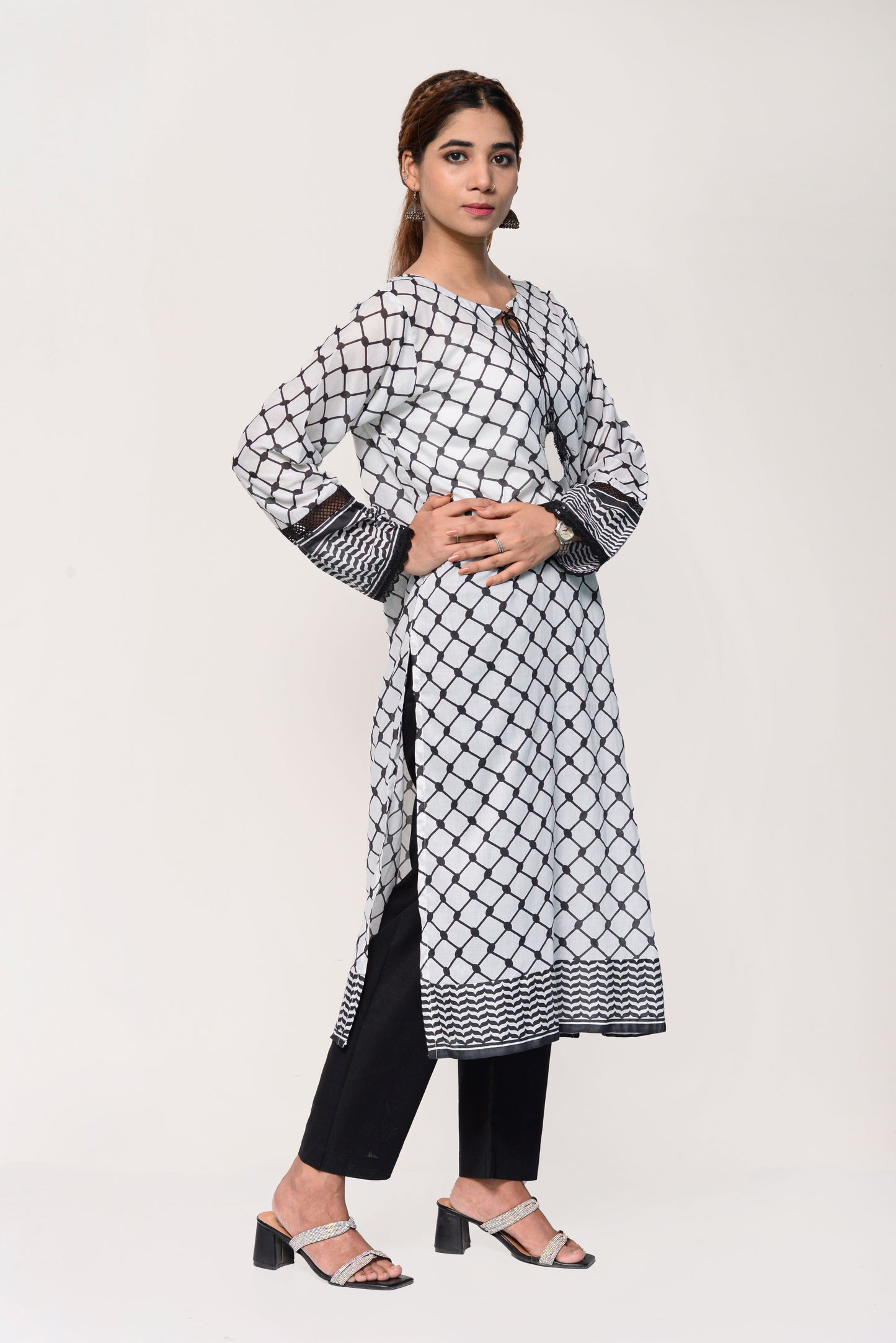 Woman wearing a black and white keffiyah patterned kurta with black pants on a light gray background