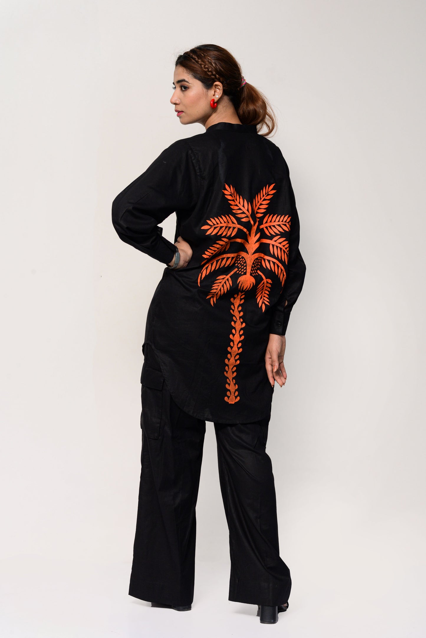 Woman wearing a black outfit with an orange palm tree design on the back against a white background