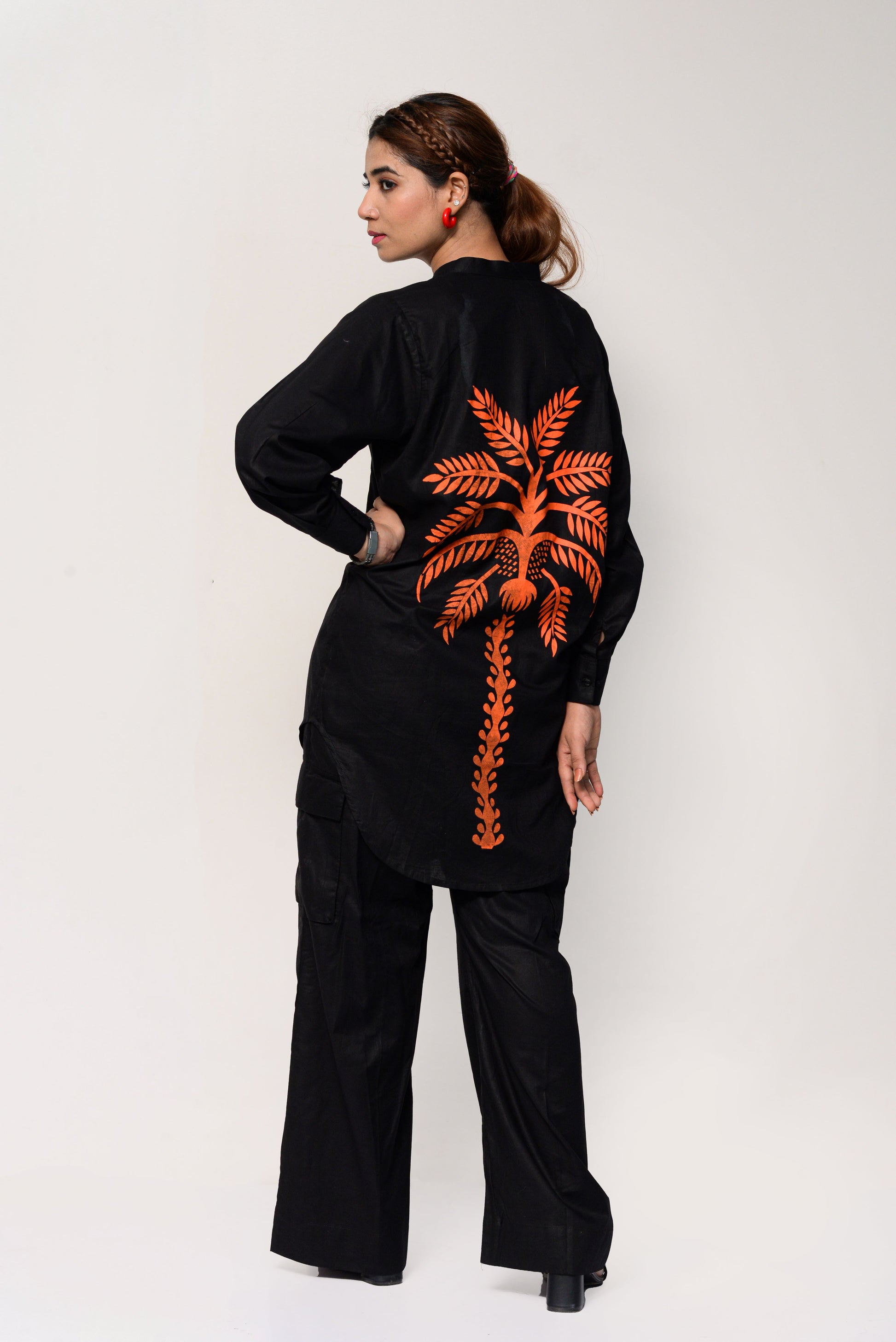 Woman wearing a black outfit with an orange palm tree design on the back against a white background